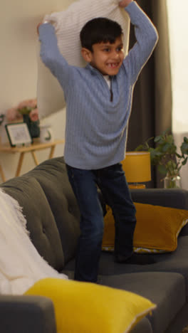 Vertical-Video-Of-Disruptive-Young-Boy-Behaving-Badly-At-Home-Jumping-On-Sofa-And-Throwing-Cushions-Around-Lounge